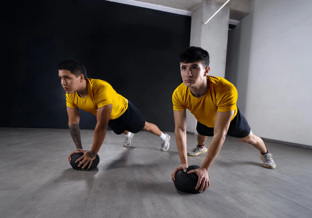 dos estudiantes de la licenciatura en ciencias del deporte de ipeth realizan planchas con apoyo en balones medicinales dentro del área de entrenamiento funcional