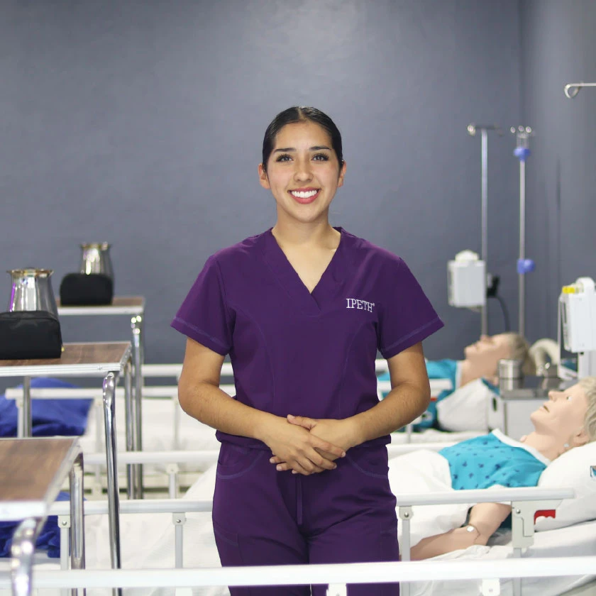 estudiante de la licenciatura en enfermería de ipeth, la universidad especializada en salud, posando en el laboratorio de simulación clínica con maniquíes hospitalarios al fondo